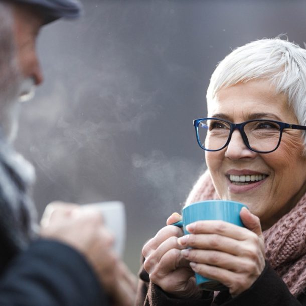 Warm into winter hero image of.an elderley couple outside in the cold enjoying a warm beverage