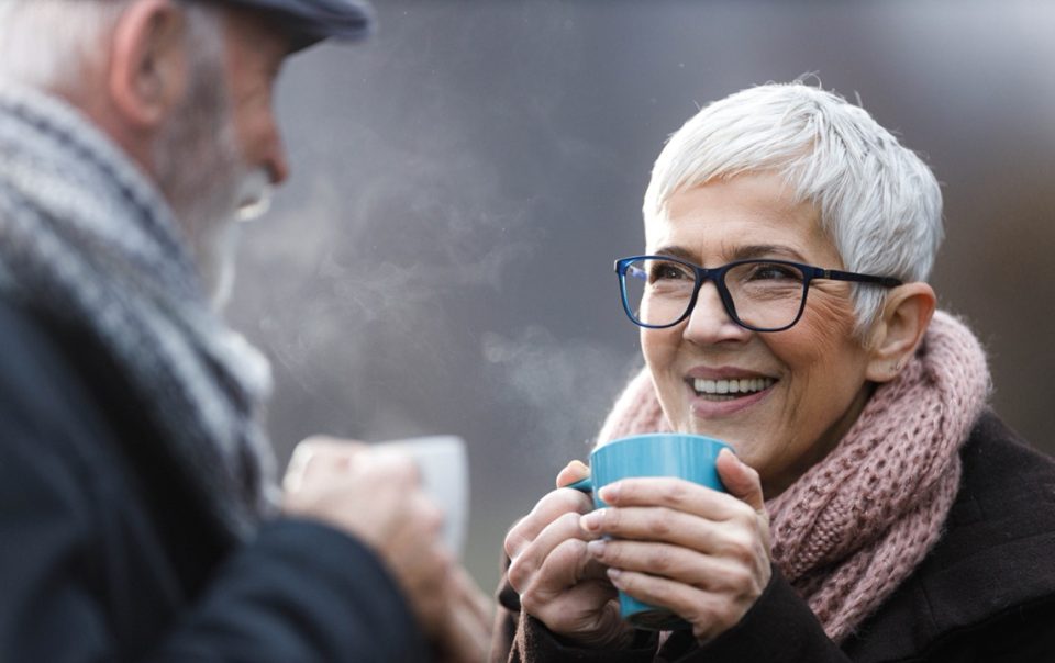 Warm into winter hero image of.an elderley couple outside in the cold enjoying a warm beverage