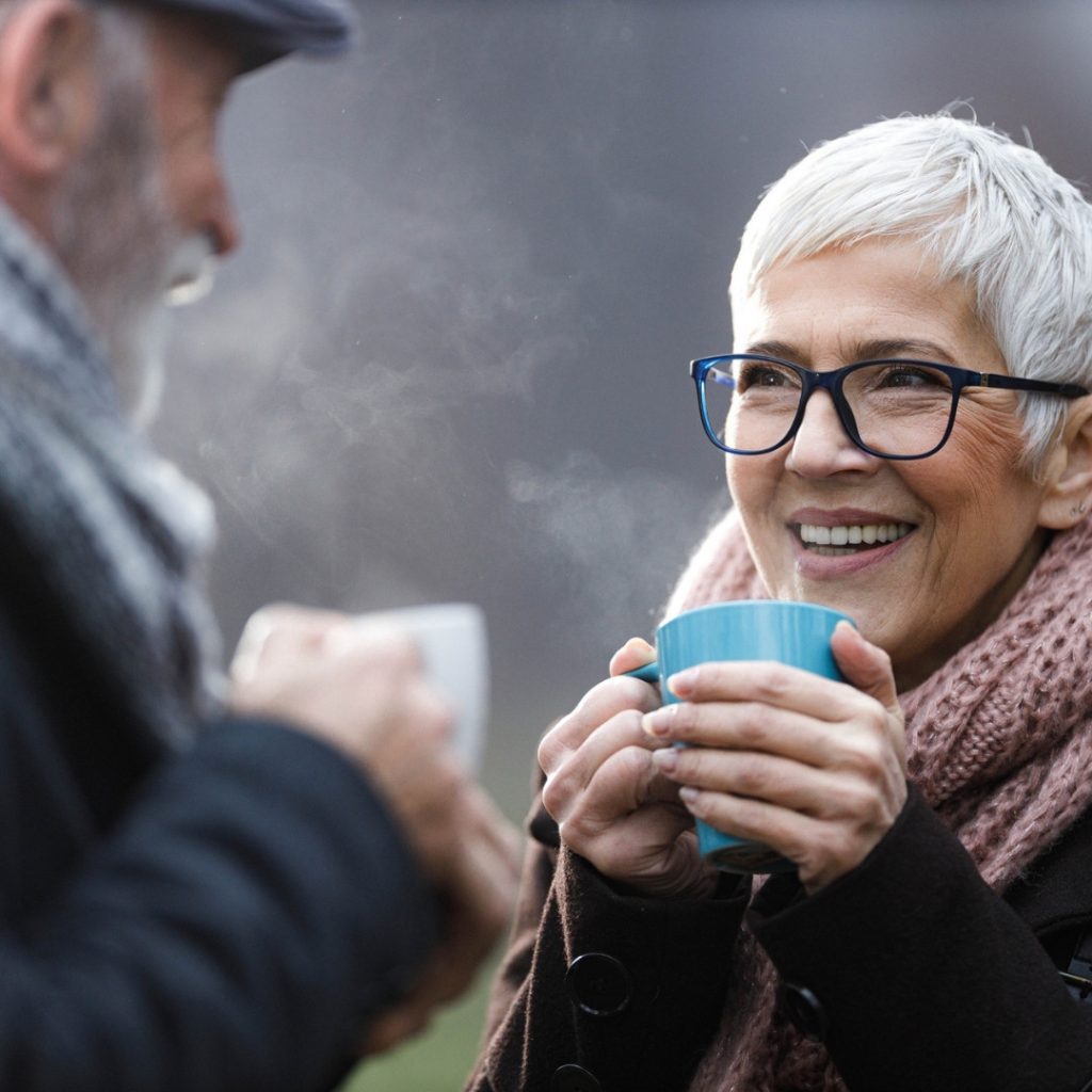 Warm into winter hero image of.an elderley couple outside in the cold enjoying a warm beverage
