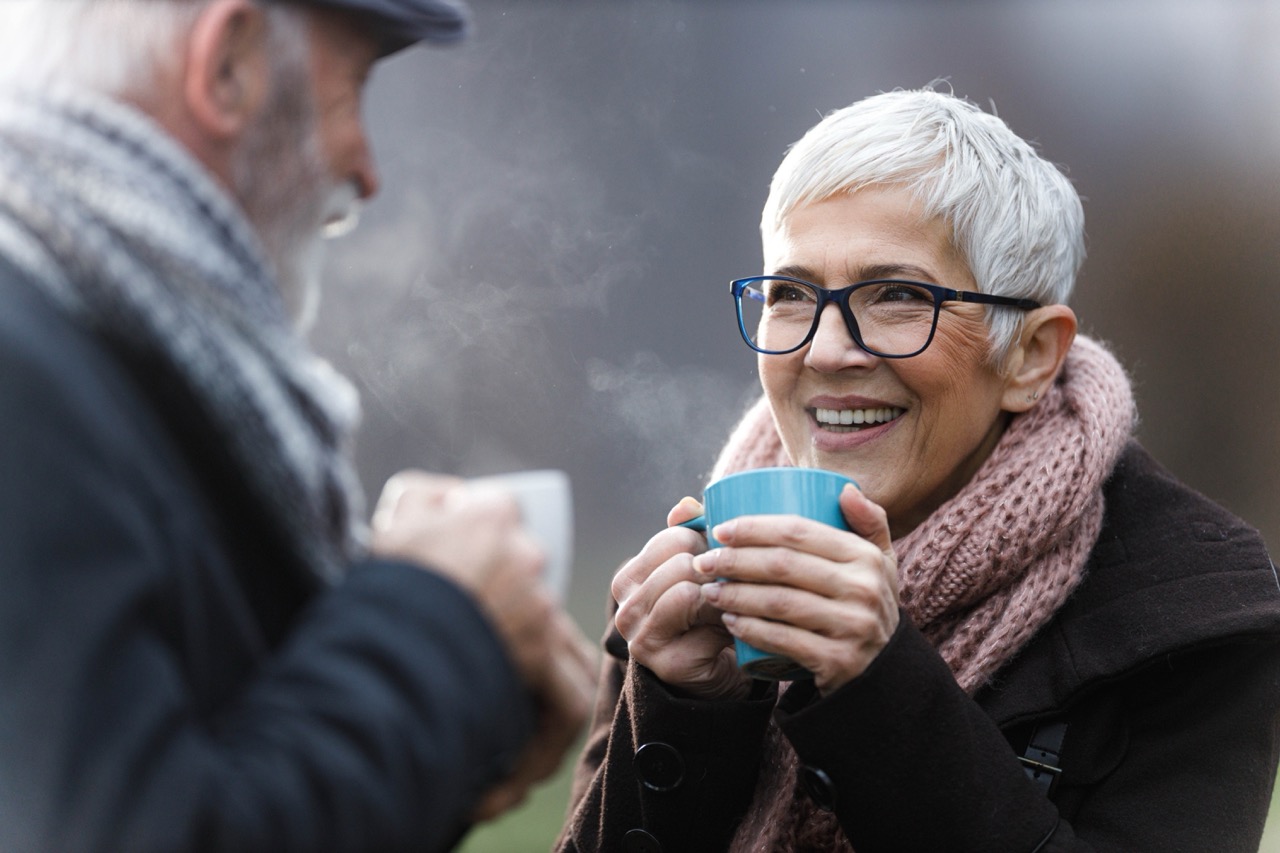 Warm into winter hero image of.an elderley couple outside in the cold enjoying a warm beverage